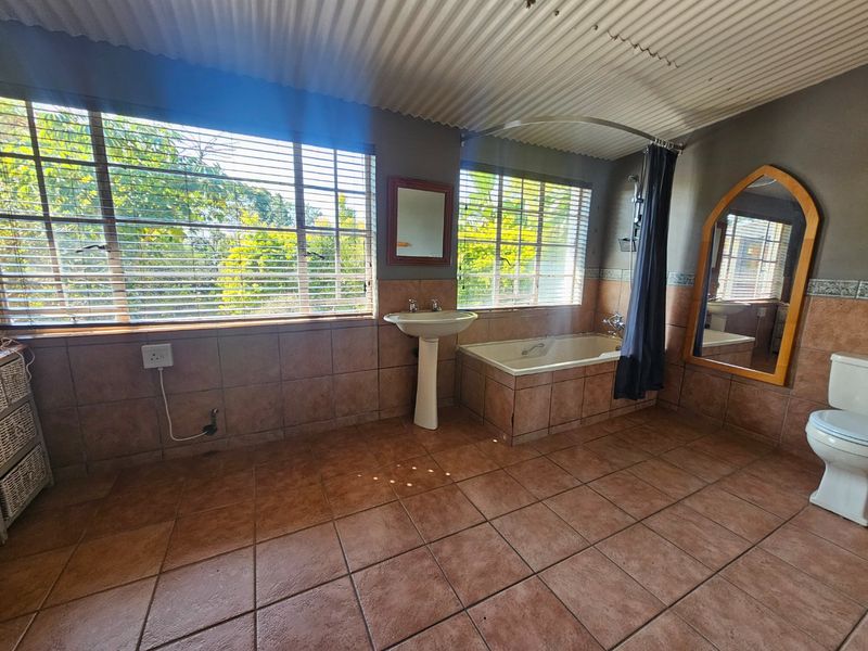Spacious bathroom featuring a pedestal basin, built-in bathtub with shower curtain, and tiled finishes throughout, offering potential for a modern renovation.