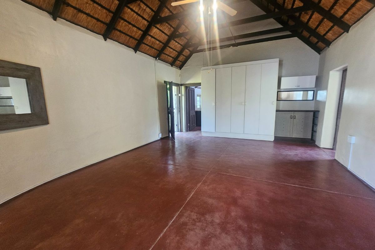 Spacious bedroom featuring a high exposed thatch ceiling, built-in cupboards, and durable screeded concrete flooring.