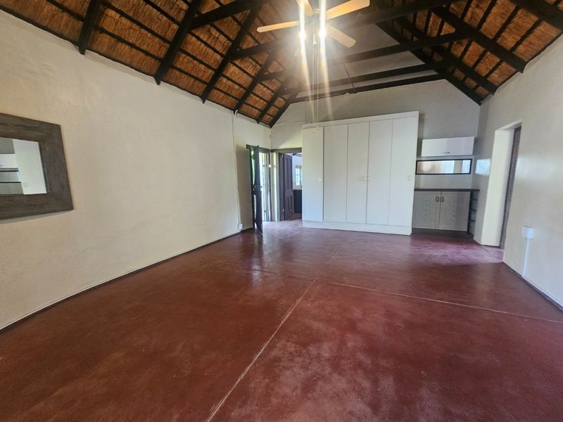 Spacious bedroom featuring a high exposed thatch ceiling, built-in cupboards, and durable screeded concrete flooring.