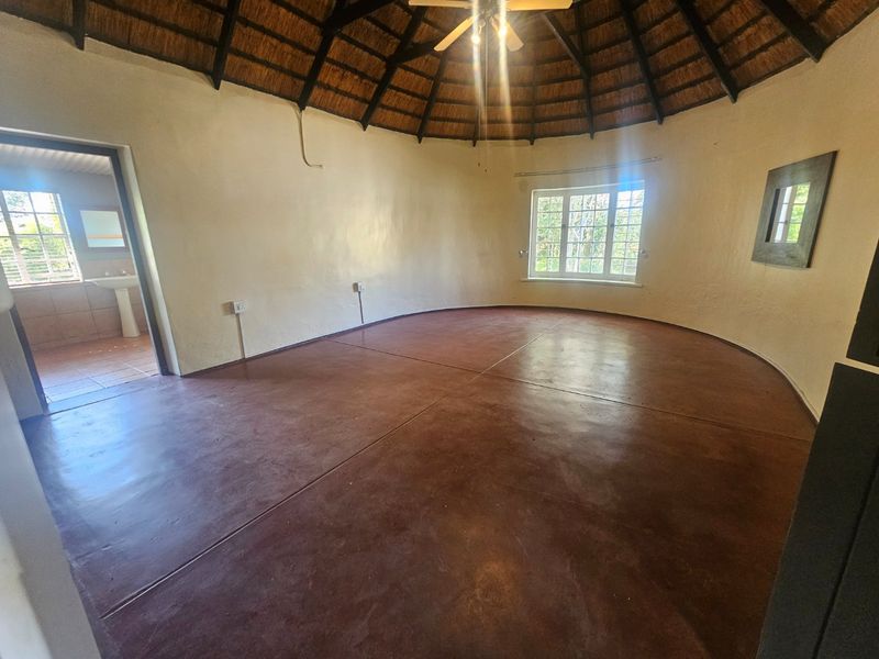 Spacious circular bedroom featuring a traditional thatched roof with exposed rafters, screeded concrete flooring, and natural light through casement windows.