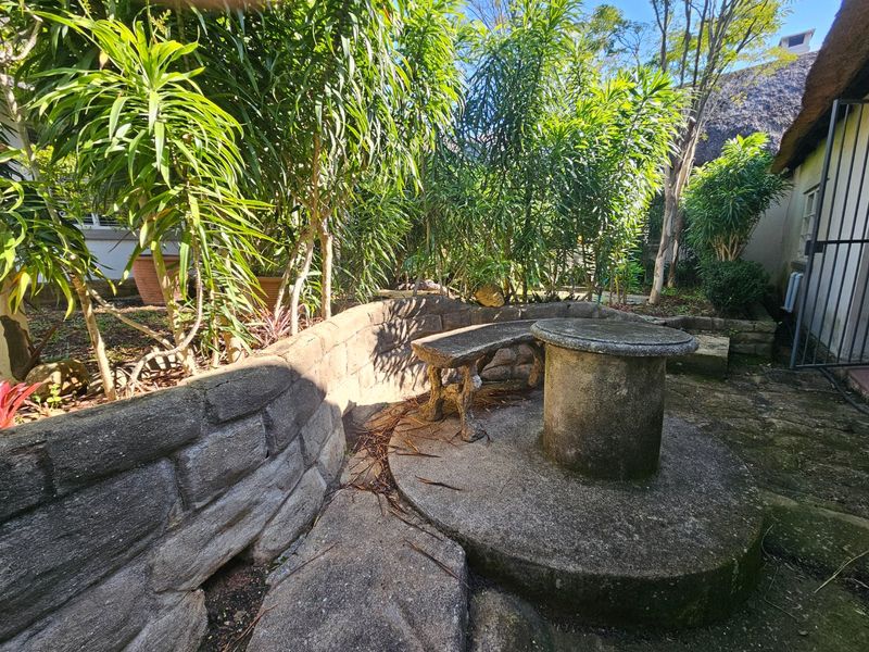 A private garden area featuring a built-in stone table and bench set against a stone retaining wall with established greenery.