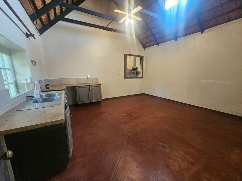 An open-plan kitchen area featuring exposed timber rafters, a high thatched ceiling, concrete flooring, and basic cabinetry with a stainless steel sink.