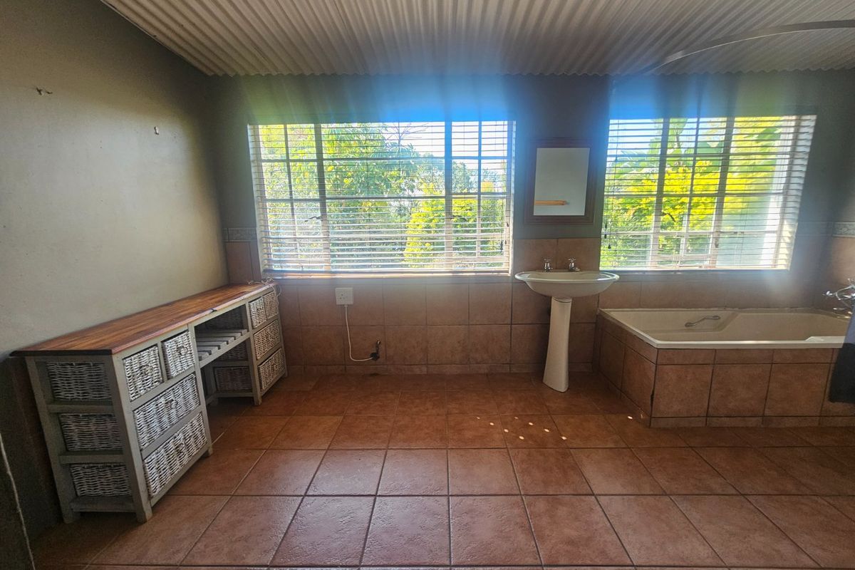 A spacious bathroom featuring a built-in bathtub, pedestal basin, tiled flooring, and large windows with venetian blinds, offering a functional layout with potential for modernization.