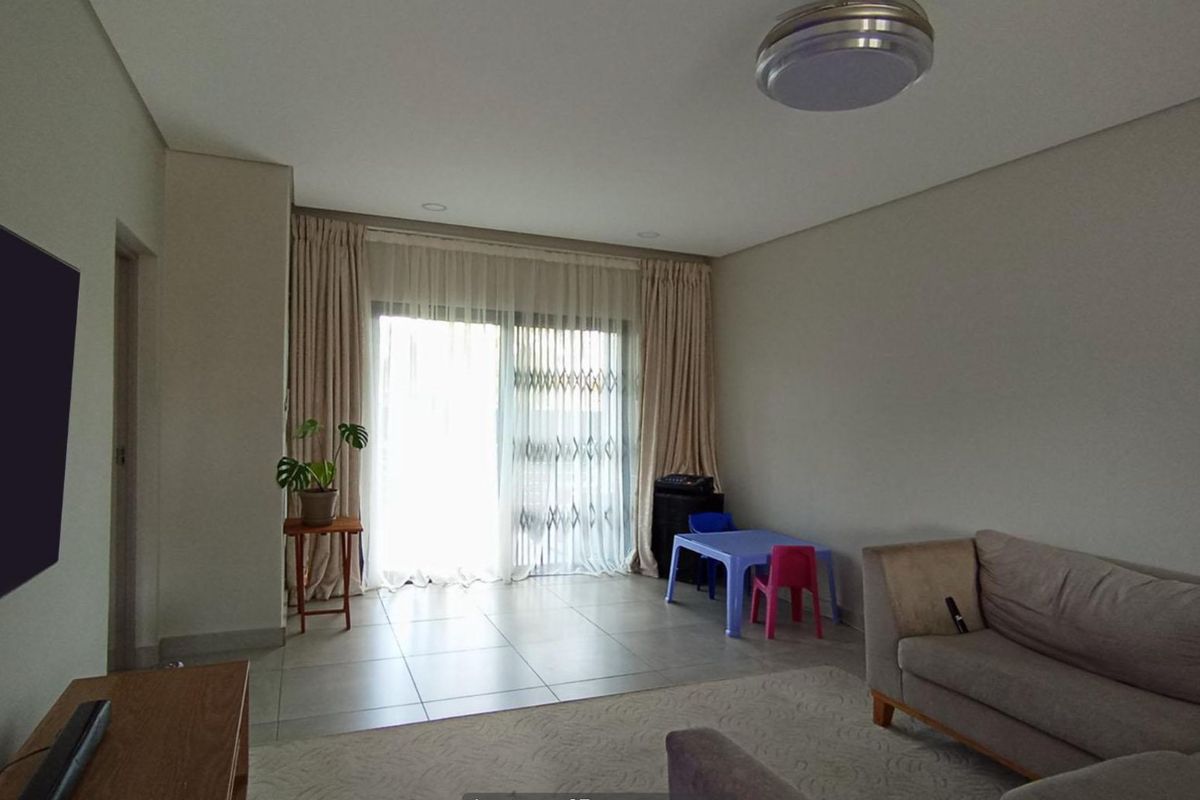 A spacious living room featuring neutral tiled flooring, recessed lighting, and a large sliding glass door providing access to the exterior.