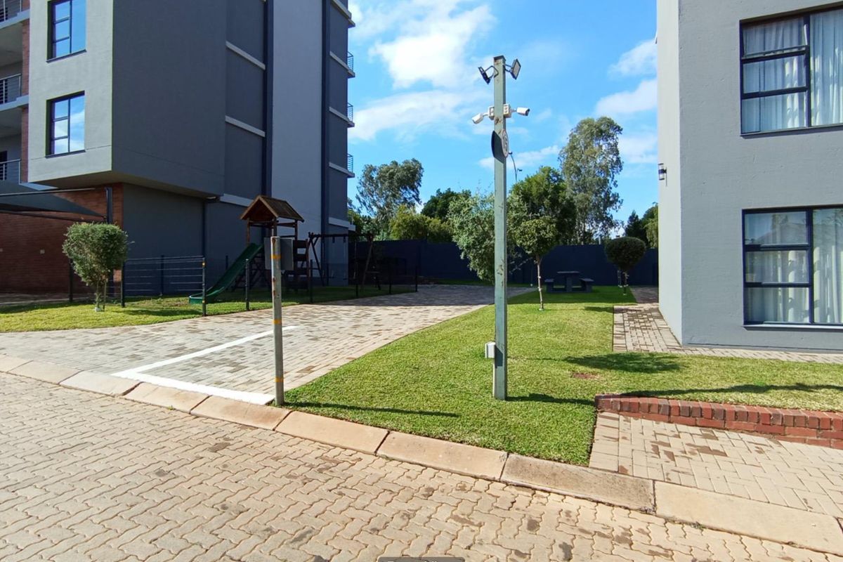 Exterior view of the apartment complex grounds featuring a paved driveway, manicured lawn, and communal children's play area.