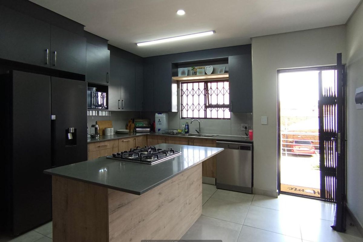 Modern kitchen featuring dark cabinetry, a central island with a gas hob, stone countertops, and direct access to the exterior via a security gate.