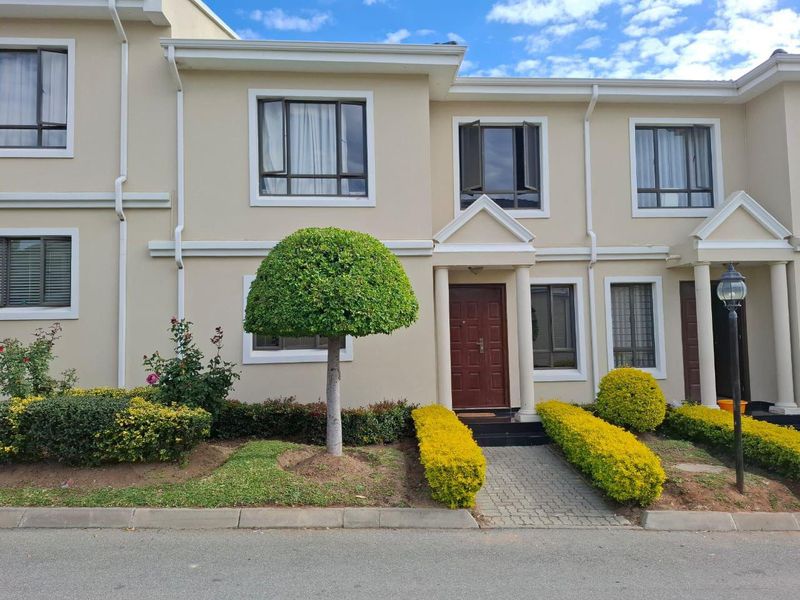 Front elevation of a well-maintained townhouse featuring a paved entrance path, manicured garden beds, and modern aluminium window frames.