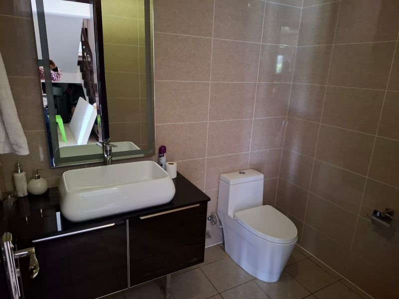 A modern bathroom featuring a vessel sink on a dark vanity cabinet, a wall-mounted mirror, and a contemporary toilet with neutral wall tiling.