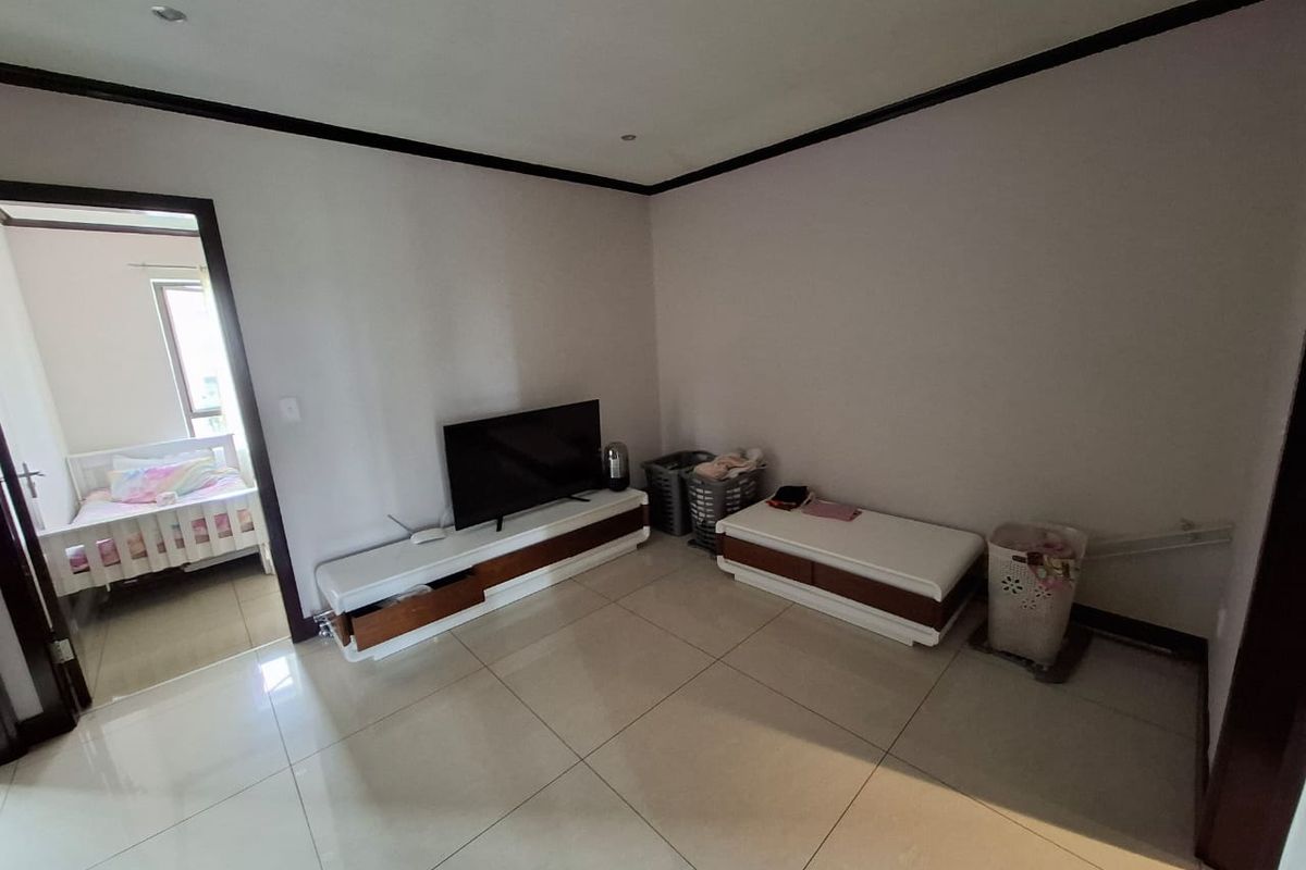 A living room area featuring large format floor tiles, recessed downlighting, and dark trim detailing, with an adjacent view into a bedroom.