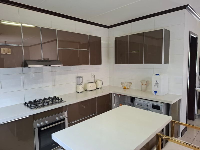 Modern kitchen featuring high-gloss brown cabinetry, stone countertops, a gas hob, built-in oven, and integrated laundry appliance.