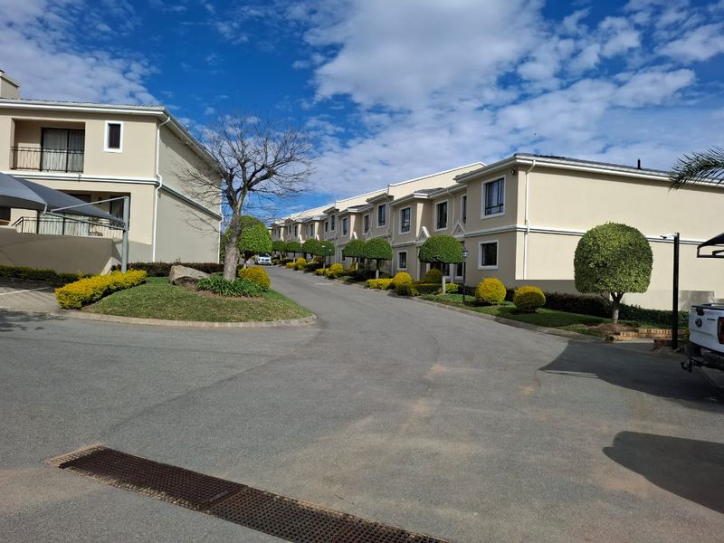 A view of the townhouse complex driveway featuring well-maintained landscaping, paved access roads, and exterior building facades.