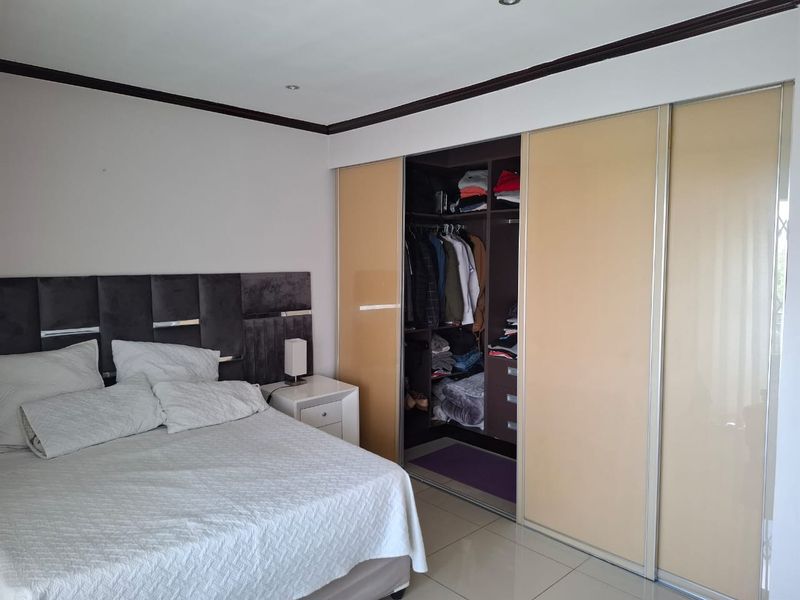 A well-maintained bedroom featuring large built-in sliding door wardrobes, tiled flooring, and recessed ceiling lighting.