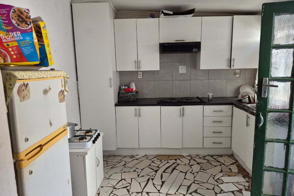 A functional kitchen featuring white cabinetry, black countertops, and a tiled backsplash, requiring some maintenance to the flooring and finishes.