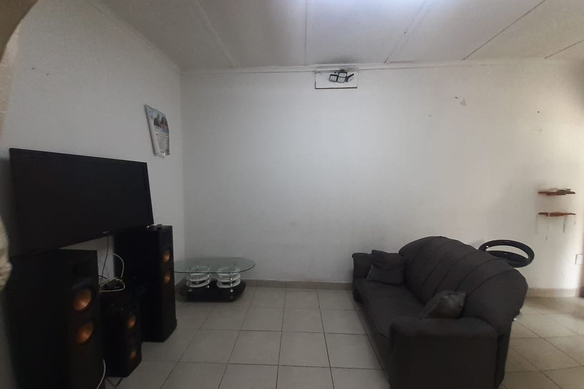A living room featuring tiled flooring and a ceiling light fixture, currently showing signs of wear on the walls and ceiling.