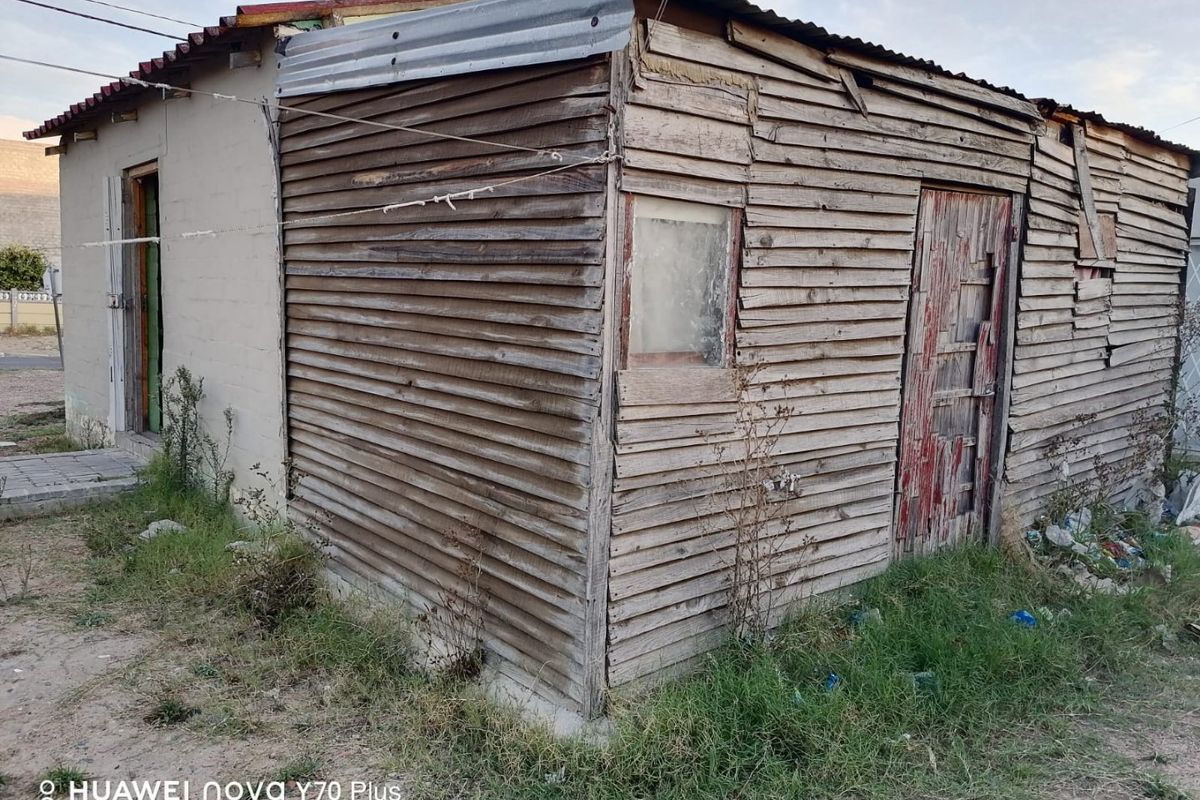 Exterior view of a small structure featuring weathered timber cladding and a corrugated metal roof, showing significant signs of age and deterioration.