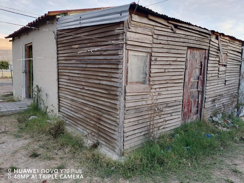 Exterior view of a small structure featuring weathered timber cladding and a corrugated metal roof, showing significant signs of age and deterioration.
