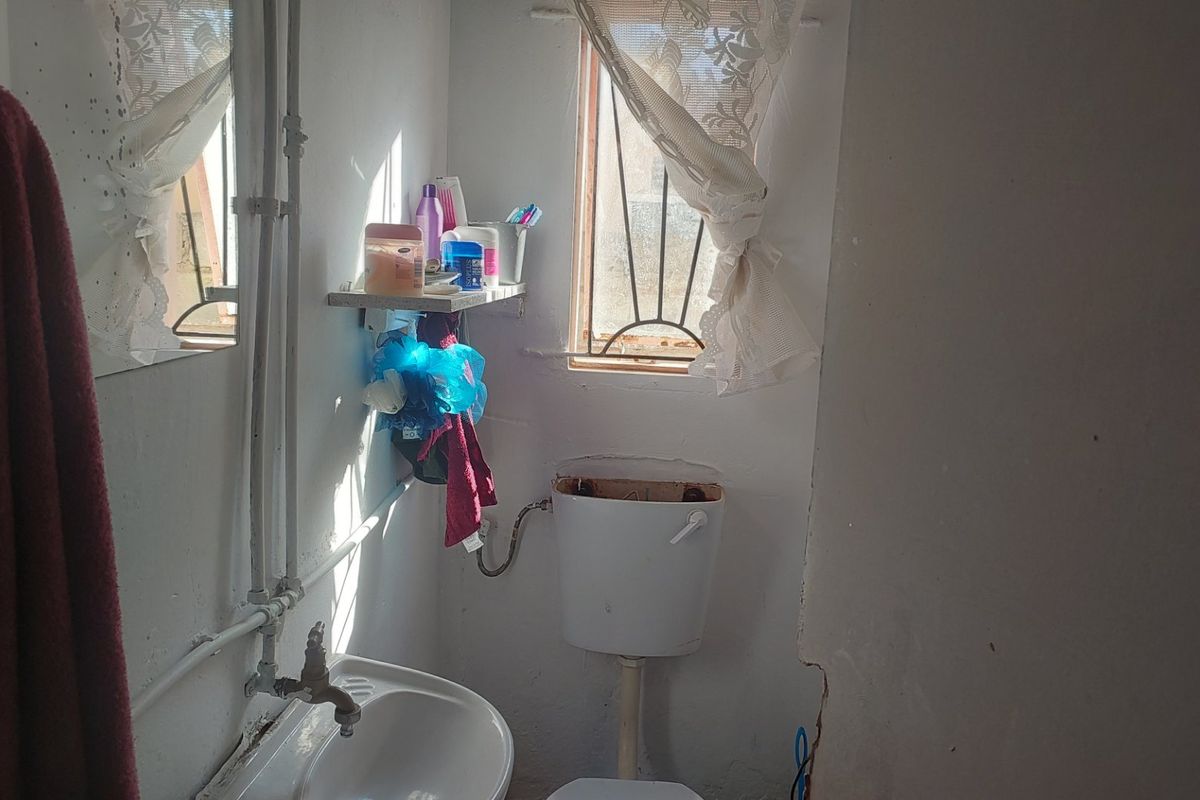 A small bathroom featuring a wall-mounted basin and toilet cistern, currently showing signs of wear and requiring maintenance or renovation.