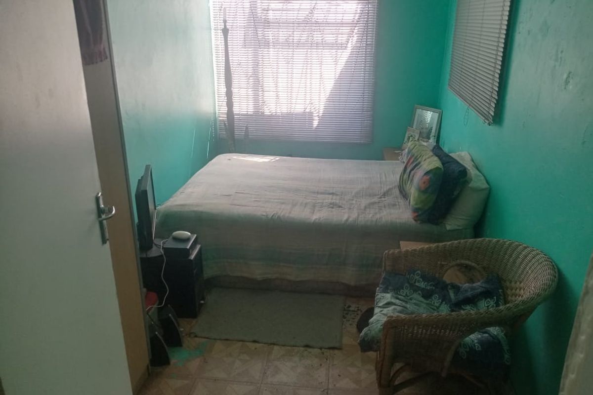 A compact bedroom featuring vinyl flooring and window blinds, currently requiring cosmetic updates and wall repairs to improve the overall living space.