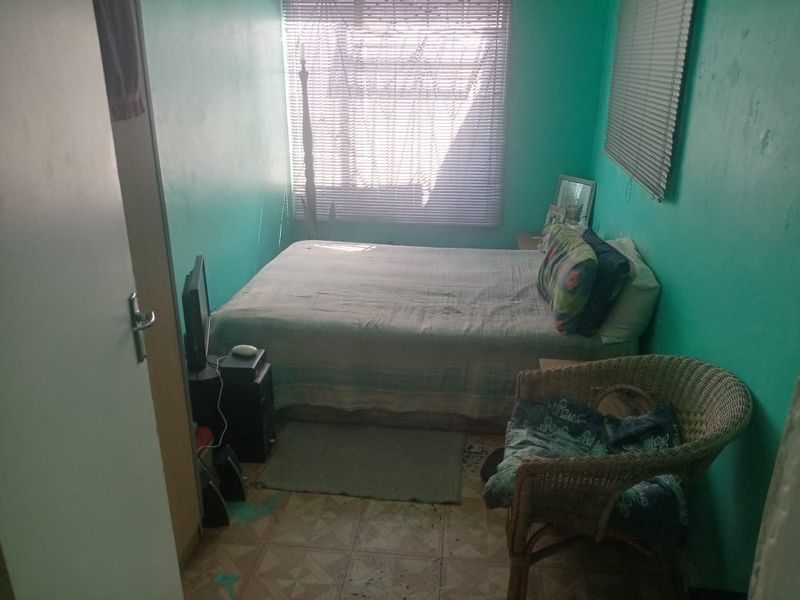 A compact bedroom featuring vinyl flooring and window blinds, currently requiring cosmetic updates and wall repairs to improve the overall living space.