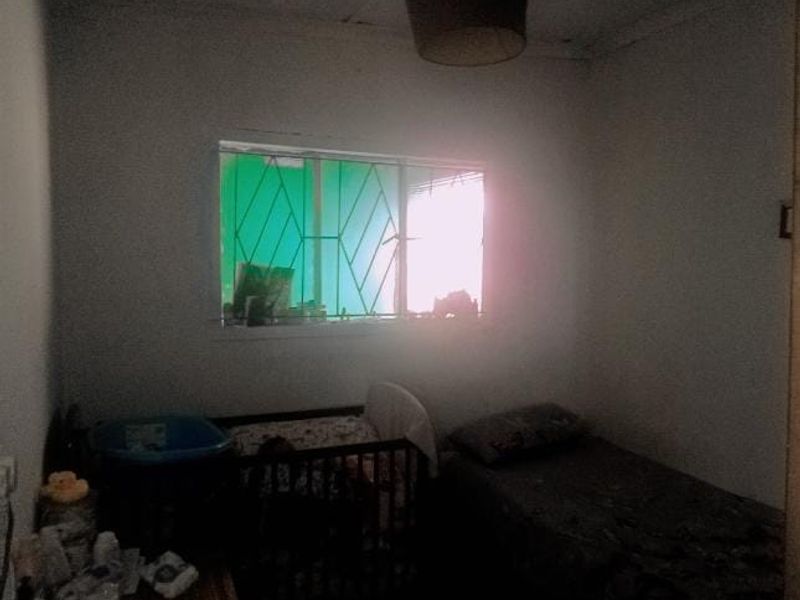A bedroom featuring security bars on the window and a central ceiling light fixture, requiring cosmetic updates to improve the overall aesthetic.