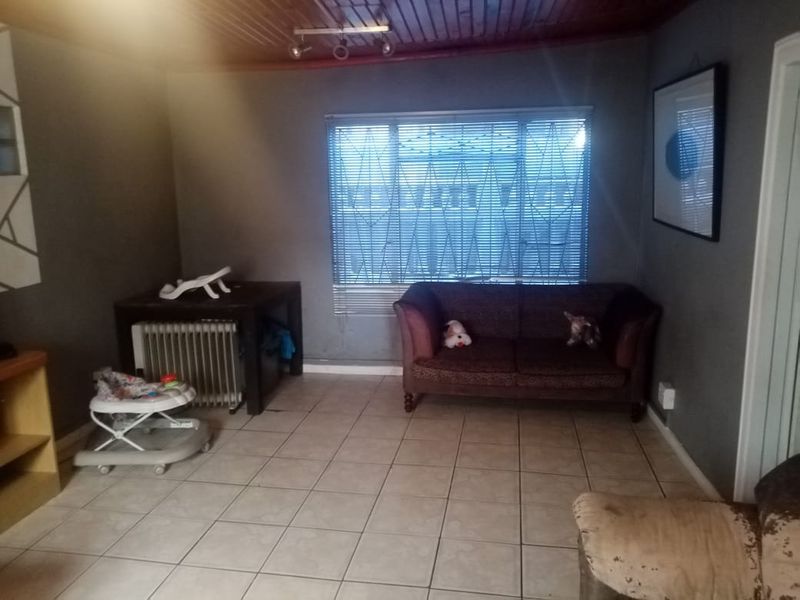 A living room featuring tiled flooring, a timber ceiling, and security bars on the window, offering a functional space with potential for modernization.