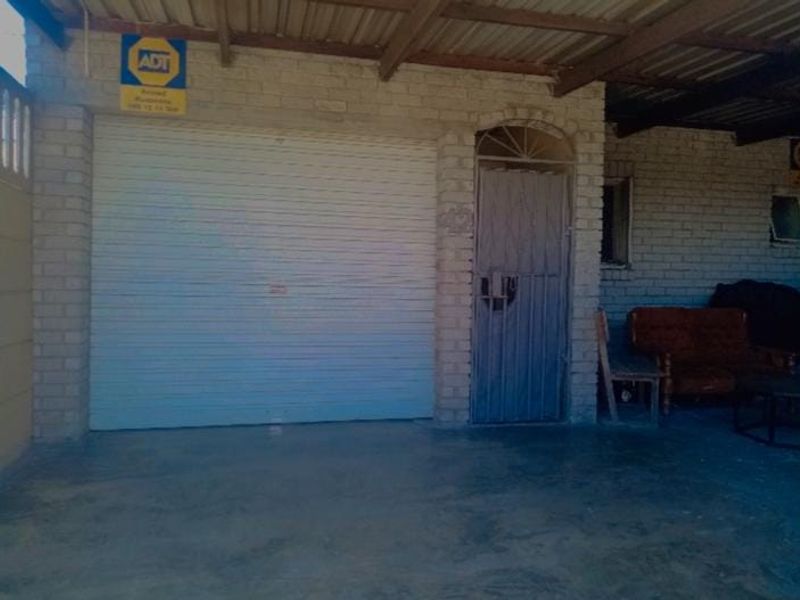 A functional garage space featuring a roller shutter door, security gate, and exposed brick walls under a corrugated roof structure.