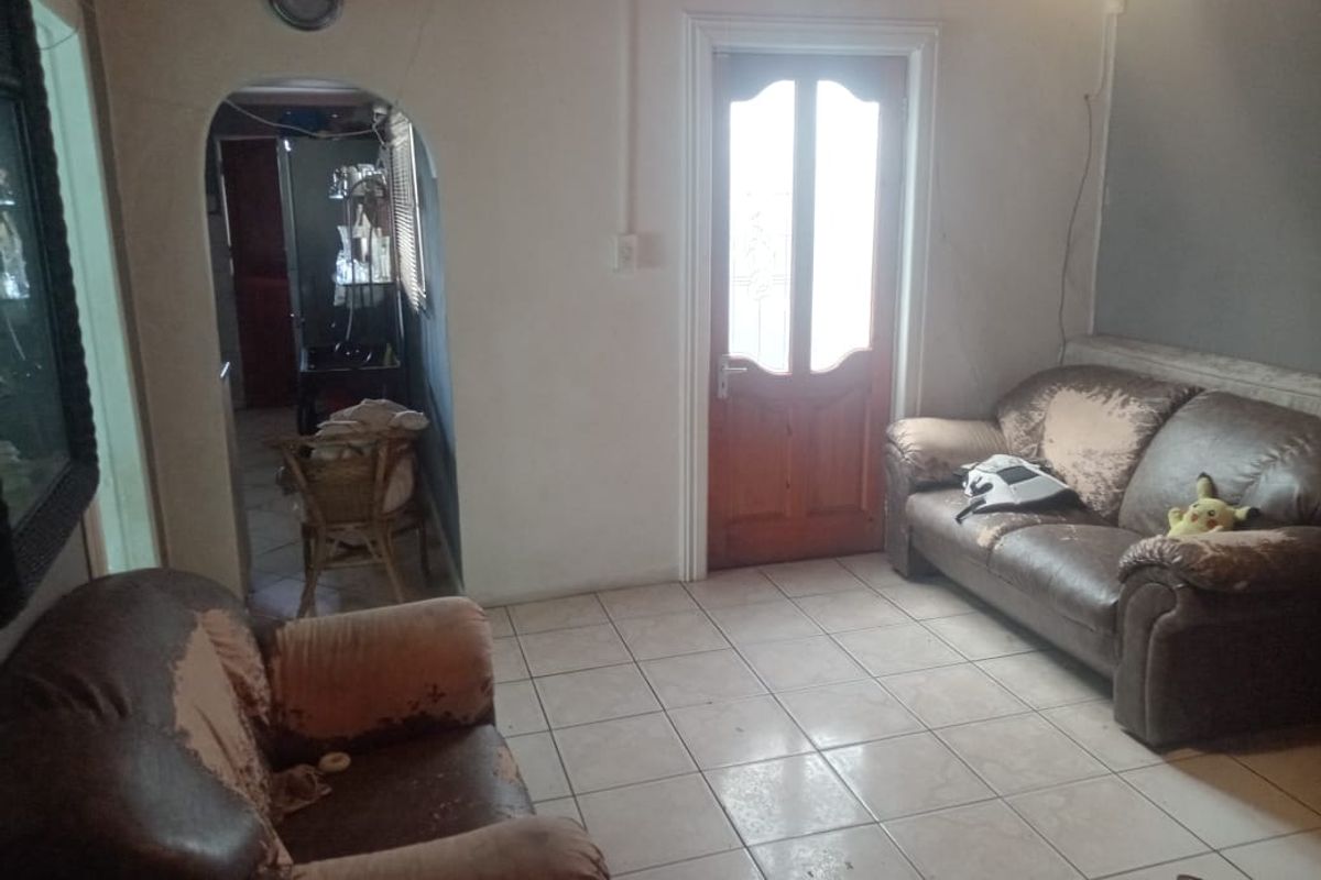 A living room area featuring tiled flooring, an arched transition to an adjacent space, and a timber entrance door.