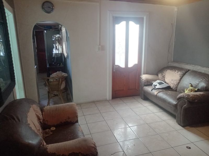 A living room area featuring tiled flooring, an arched transition to an adjacent space, and a timber entrance door.