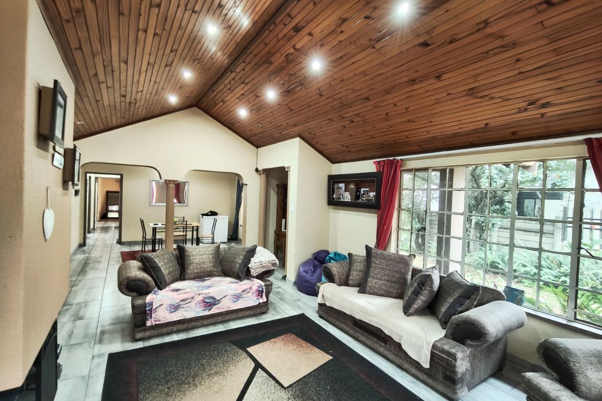 Spacious living room featuring a vaulted timber ceiling, recessed lighting, and large windows overlooking the garden, with tiled flooring throughout.