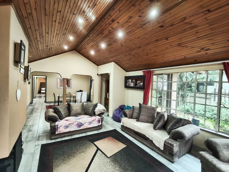 Spacious living room featuring a vaulted timber ceiling, recessed lighting, and large windows overlooking the garden, with tiled flooring throughout.