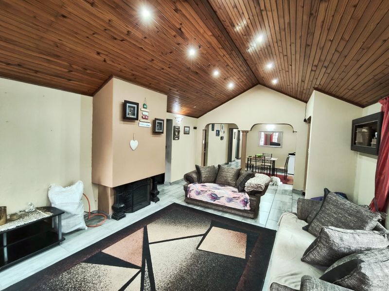 Spacious living room featuring a high timber-clad vaulted ceiling, recessed lighting, tiled flooring, and a built-in fireplace with arched transitions to adjacent areas.