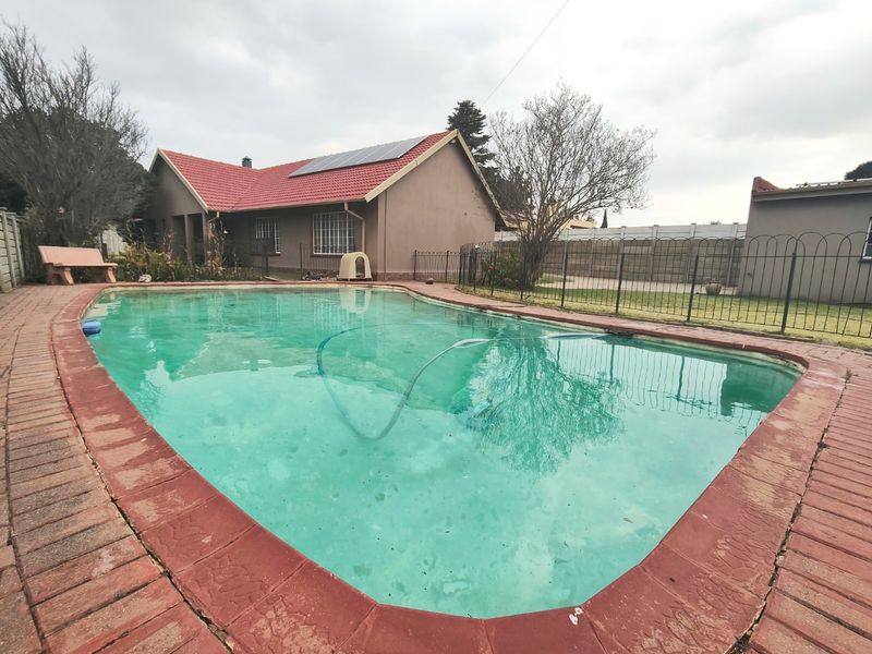 Rear garden area featuring a swimming pool with brick coping, solar panels on the roof, and metal perimeter fencing.