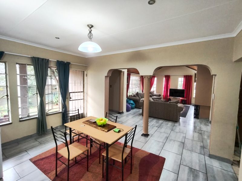 Open-plan living and dining area featuring tiled flooring, decorative arched columns, and ample natural light through large windows.