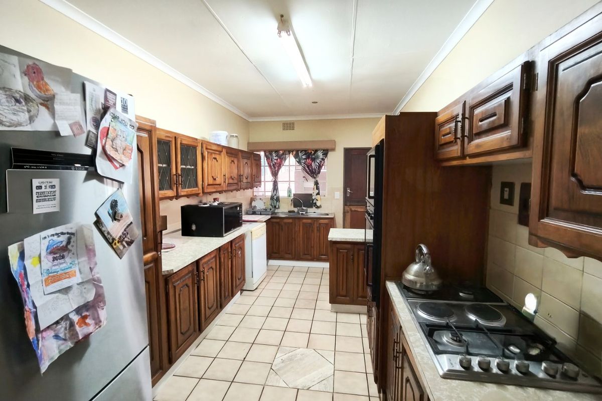 A functional galley-style kitchen featuring traditional wooden cabinetry, built-in oven, gas hob, and tiled flooring, offering a classic layout with ample storage space.