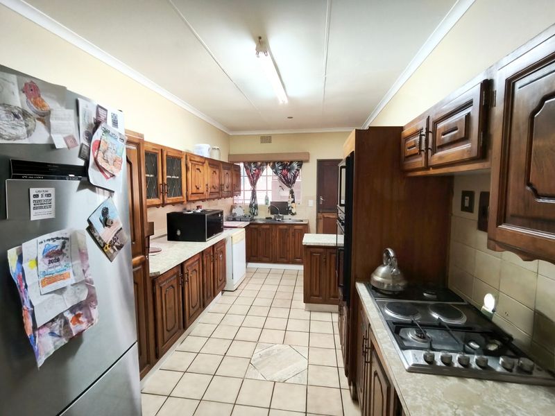 A functional galley-style kitchen featuring traditional wooden cabinetry, built-in oven, gas hob, and tiled flooring, offering a classic layout with ample storage space.