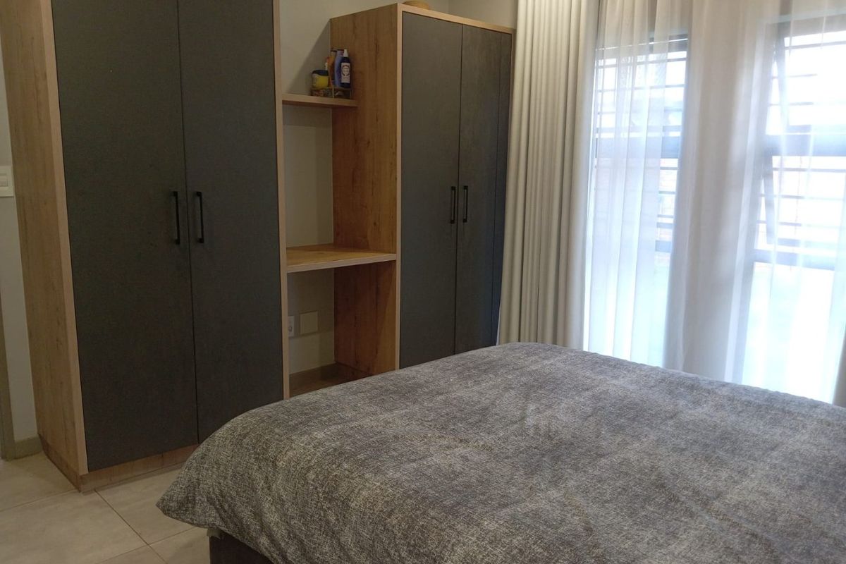 A well-maintained bedroom featuring modern built-in cupboards with integrated shelving and tiled flooring, offering a clean and functional living space.