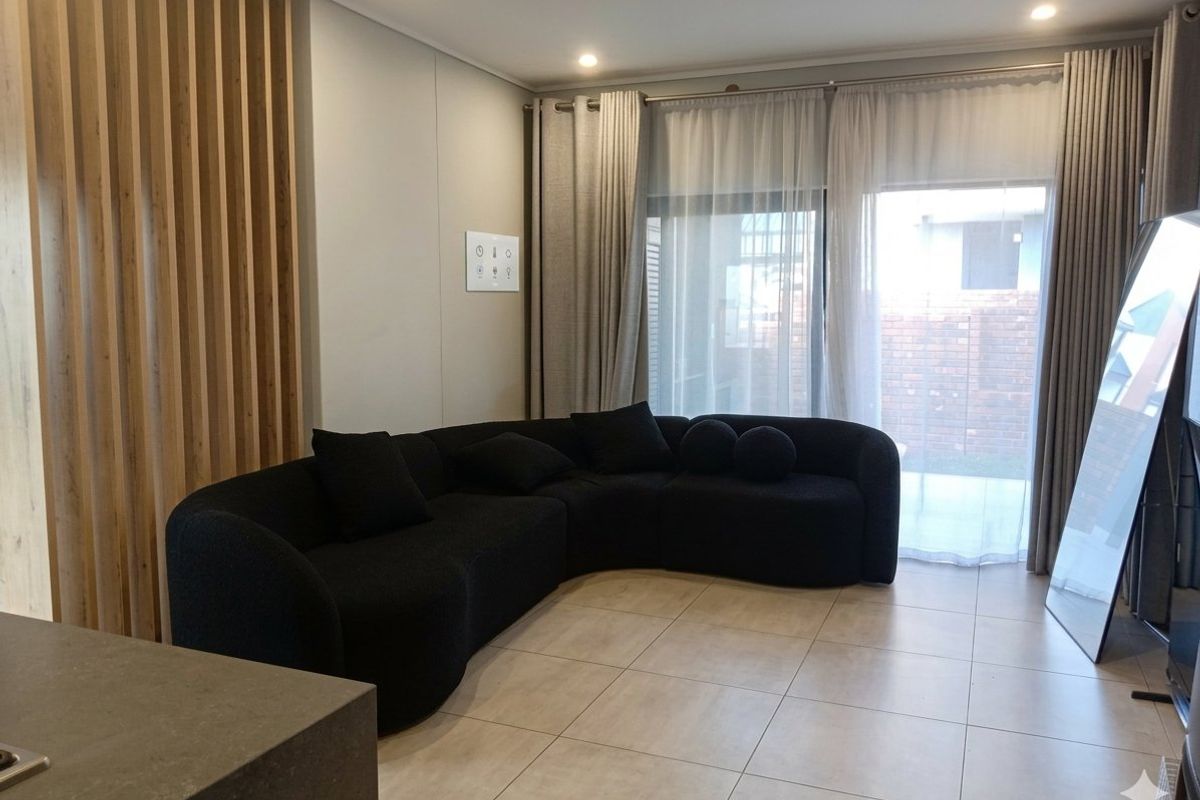 A modern living room featuring tiled flooring, recessed lighting, and a decorative timber slat partition, with direct access to the outdoor area via sliding doors.
