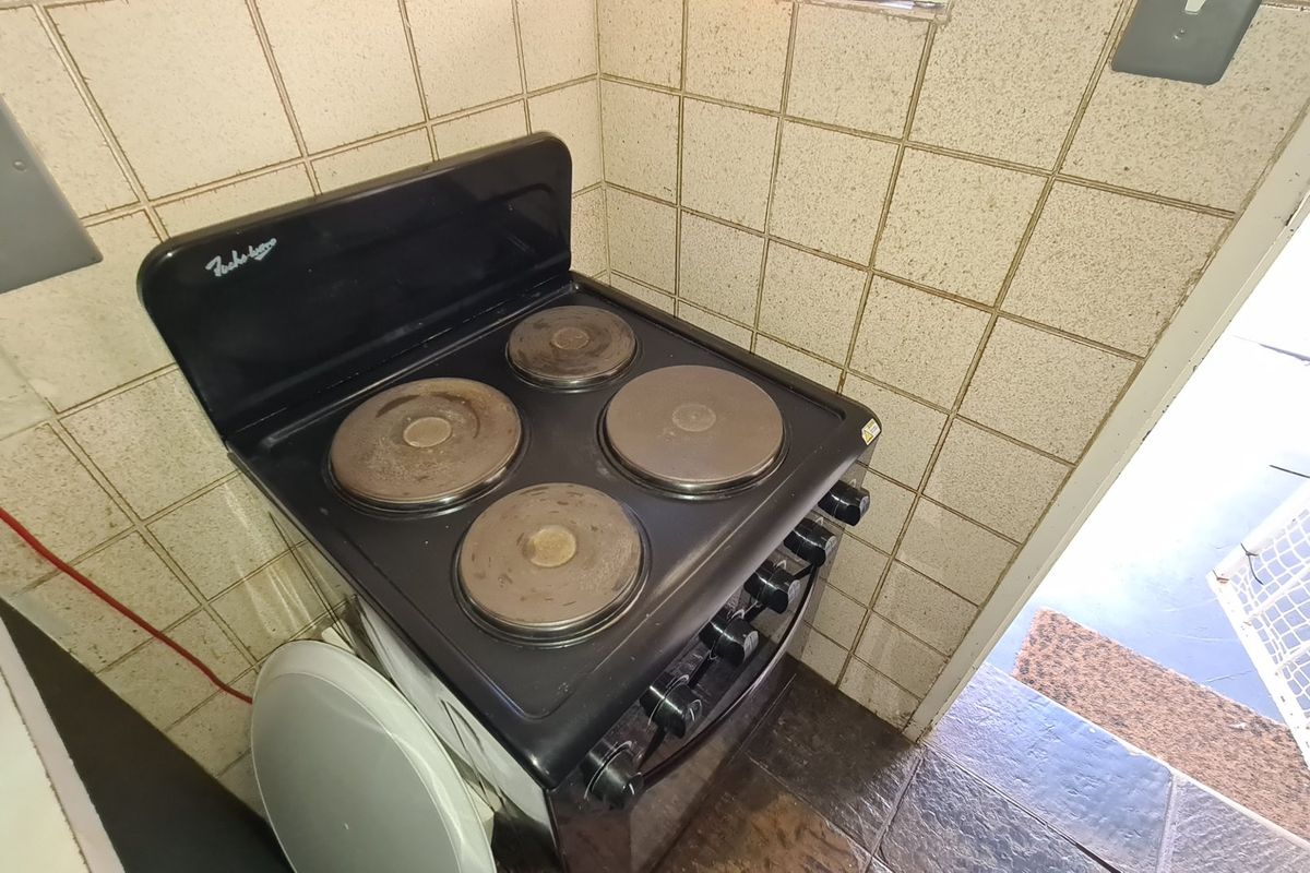 A compact kitchen corner featuring a freestanding electric stove set against tiled walls, showing signs of wear and dated finishes.