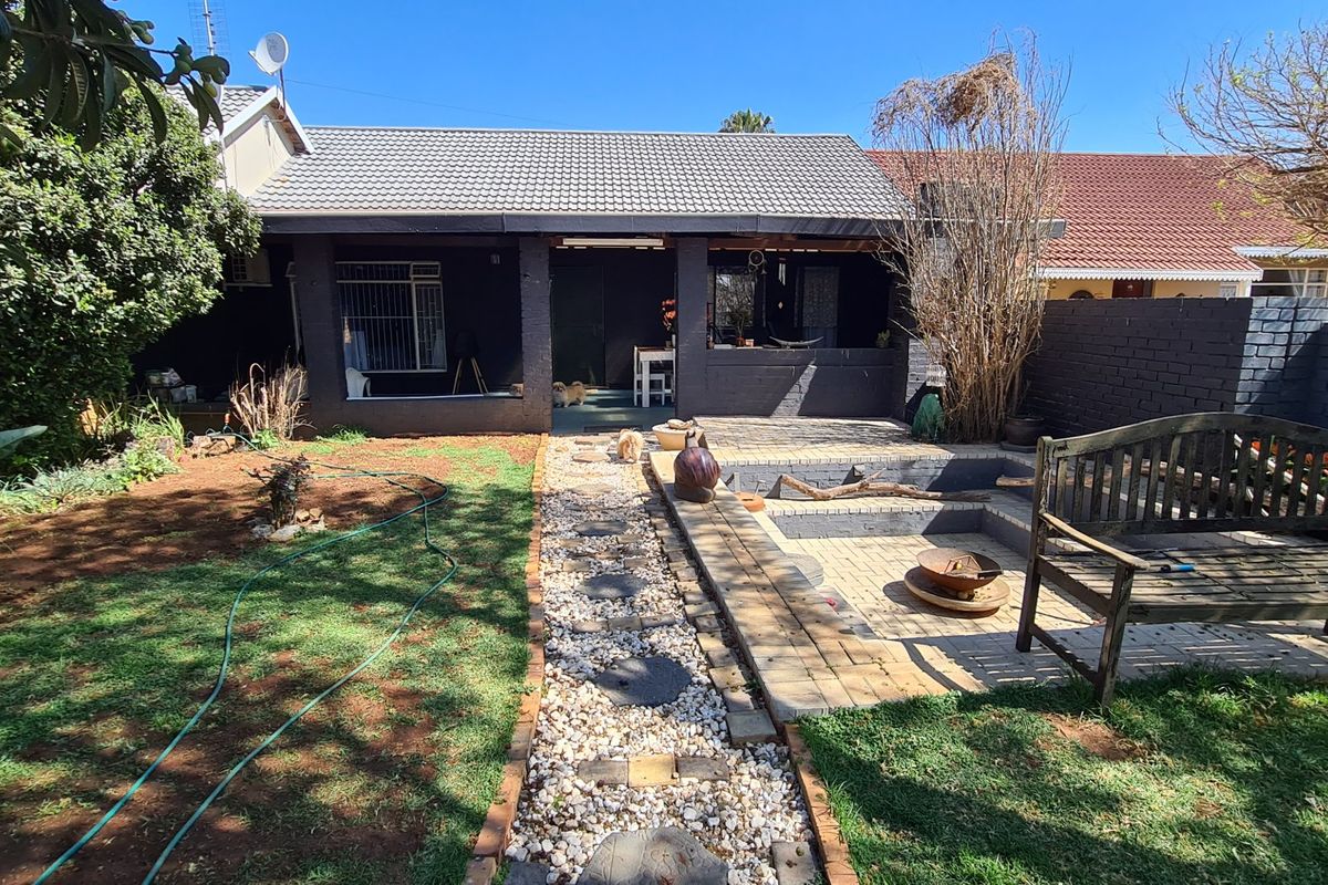 Rear exterior view featuring a covered patio, brick-paved courtyard with a sunken fire pit area, and a landscaped garden with a stone pathway.