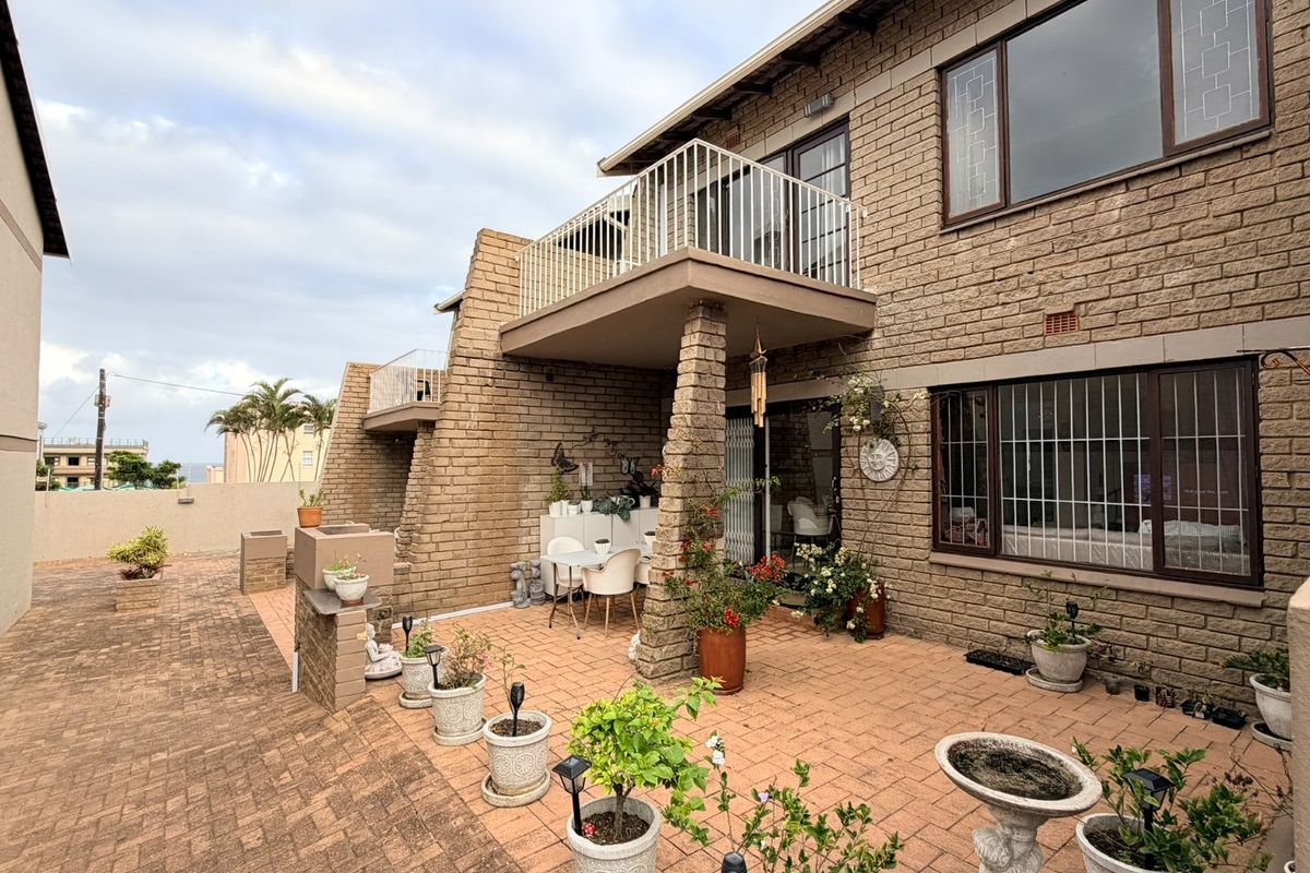 Rear exterior view of a townhouse featuring a paved patio area, brick facade, and an upper-level balcony with metal railings.