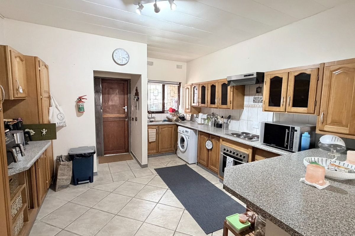 Functional kitchen featuring wooden cabinetry, granite countertops, built-in oven, hob, and extractor fan, with tiled flooring and direct access to an exterior door.