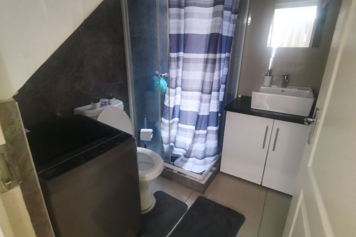 Compact bathroom featuring a shower enclosure, vanity cabinet with vessel sink, and toilet, finished with tiled walls and flooring.
