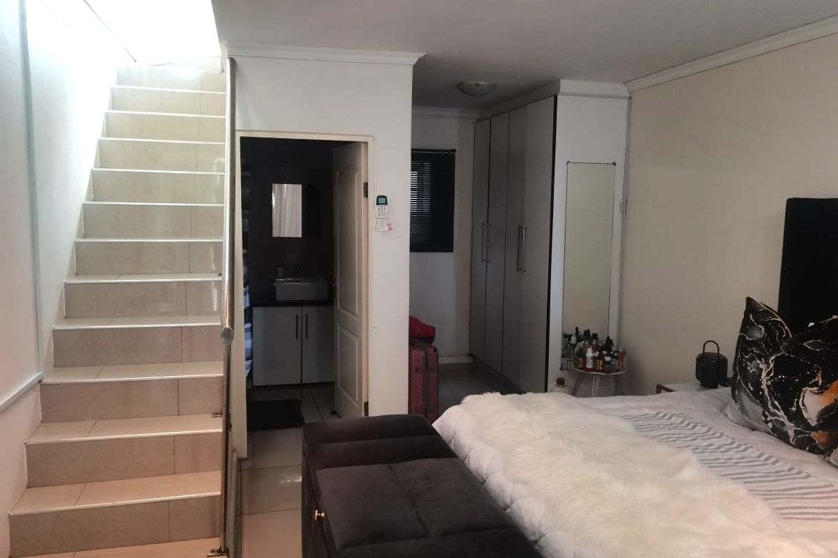 A bedroom featuring a tiled staircase leading to an upper level, built-in cupboards, and direct access to an en-suite bathroom.