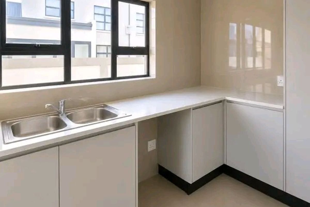 A modern, clean kitchen featuring neutral cabinetry, stone countertops, a double bowl sink, and tiled flooring, offering a bright and functional workspace.
