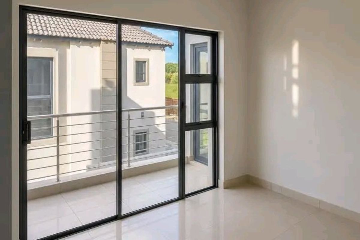 A bright, empty bedroom featuring neutral tiled floors, recessed lighting, and a large sliding glass door providing access to a private balcony.