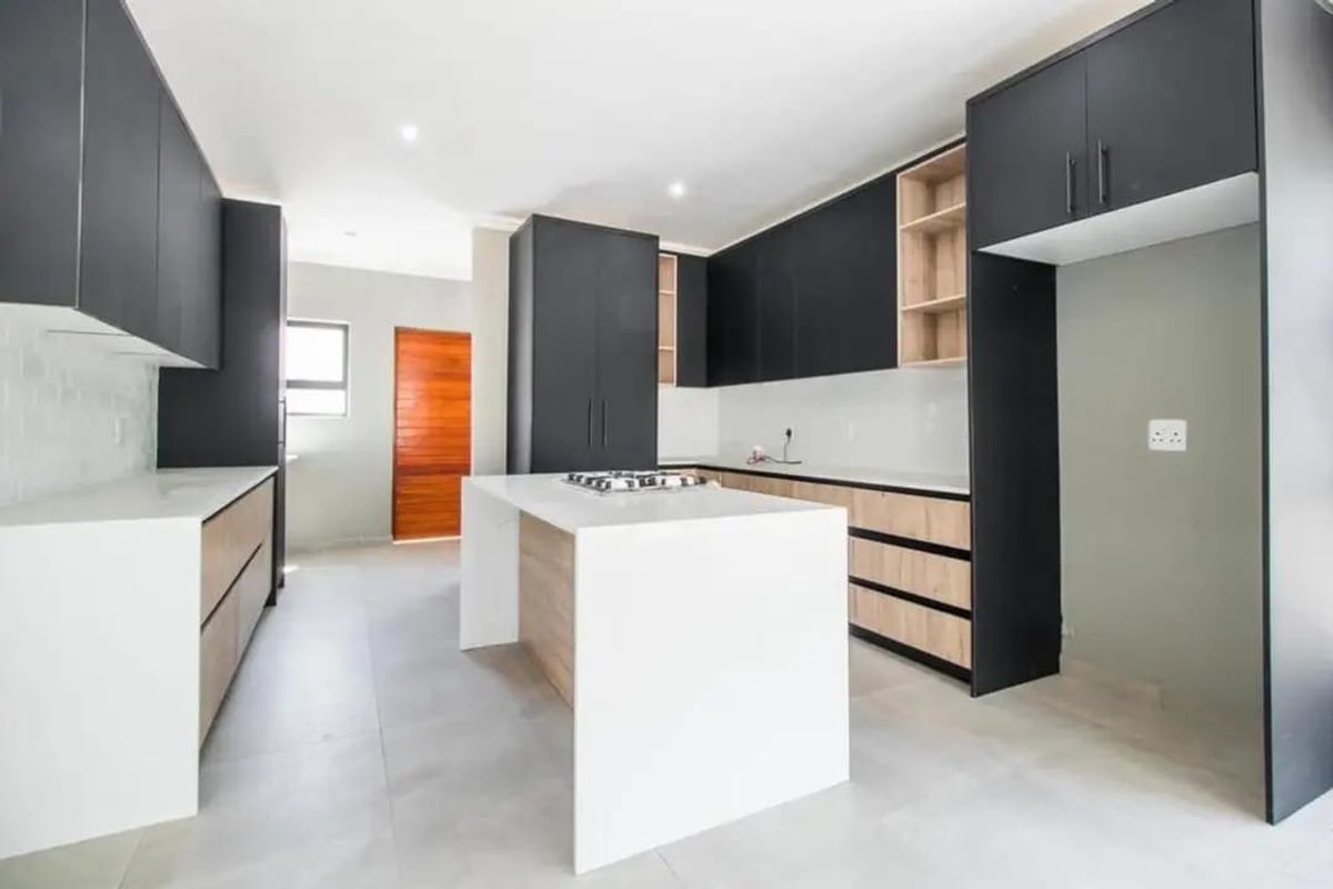 Modern kitchen featuring a central island, sleek matte black and wood-tone cabinetry, stone countertops, and integrated gas hob with neutral tiled flooring.
