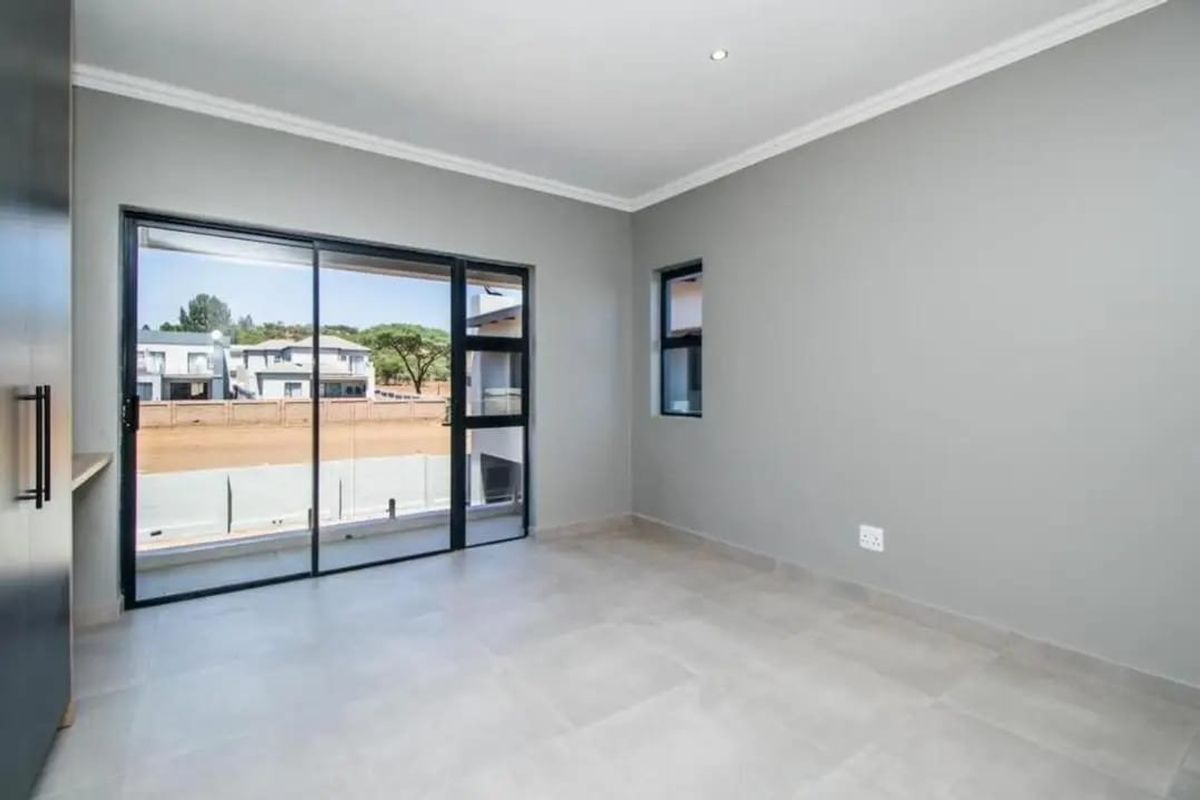 A bright, modern, and empty bedroom featuring neutral tiled floors, built-in cabinetry, and a large sliding glass door leading to an outdoor balcony.