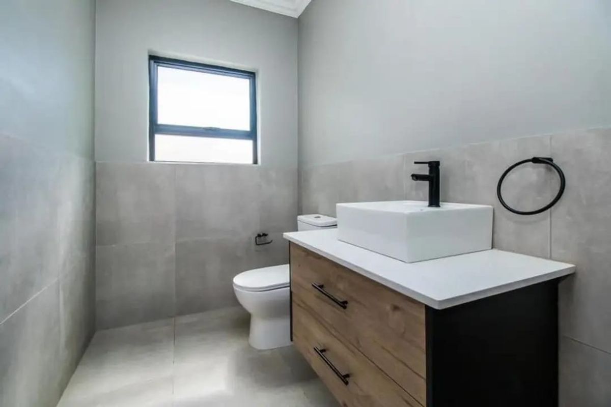 Modern bathroom featuring a contemporary vanity with vessel sink, black fixtures, and neutral grey wall and floor tiling.