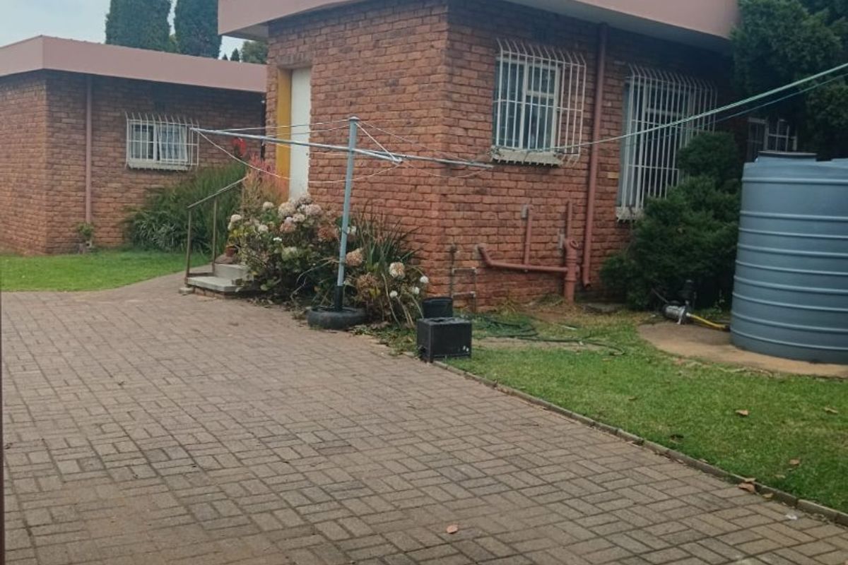 Rear view of a face brick house featuring a paved driveway, security bars on windows, and an external water storage tank.