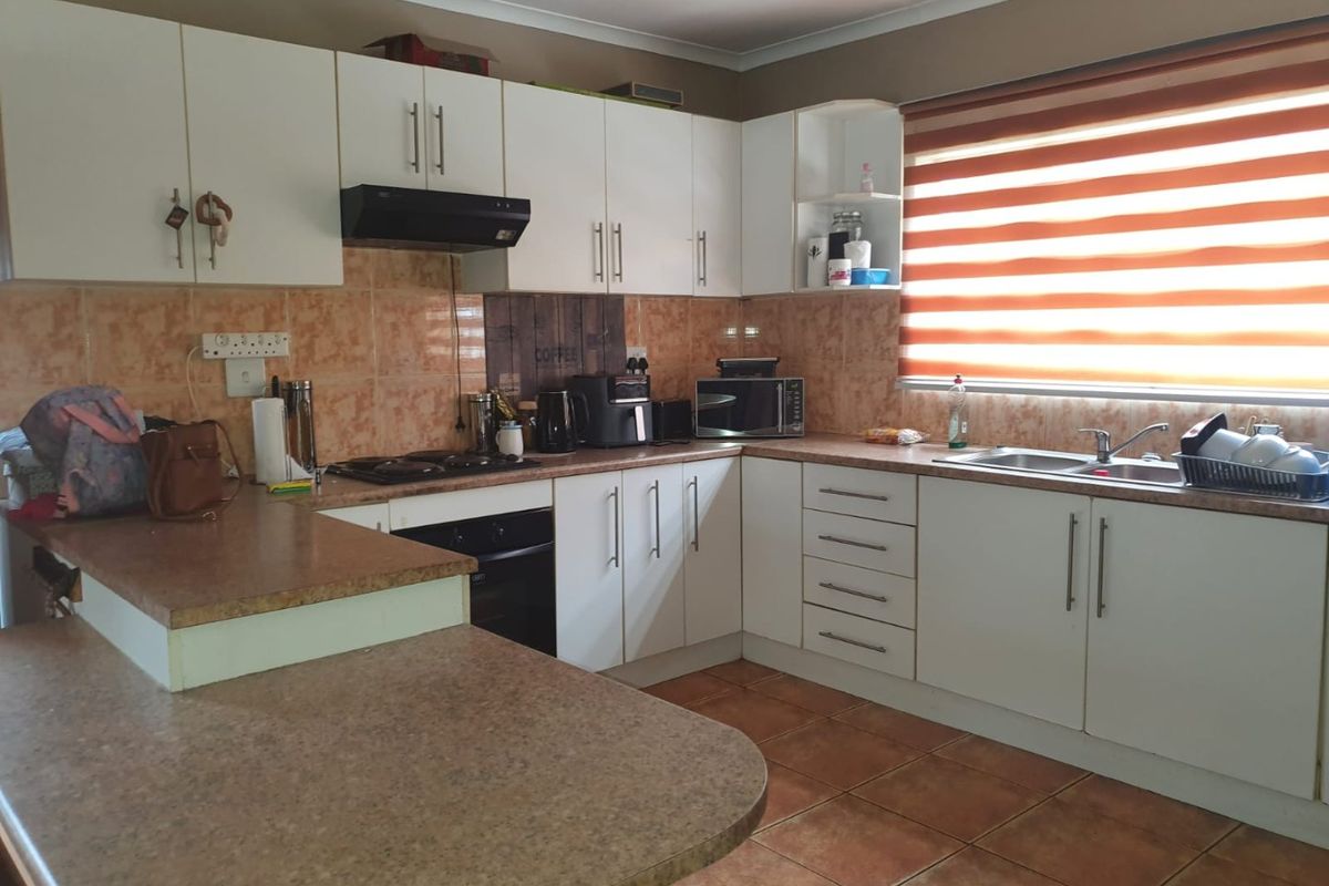Functional kitchen featuring white cabinetry, laminate countertops, built-in oven with gas hob, extractor fan, and double basin sink with tiled finishes.